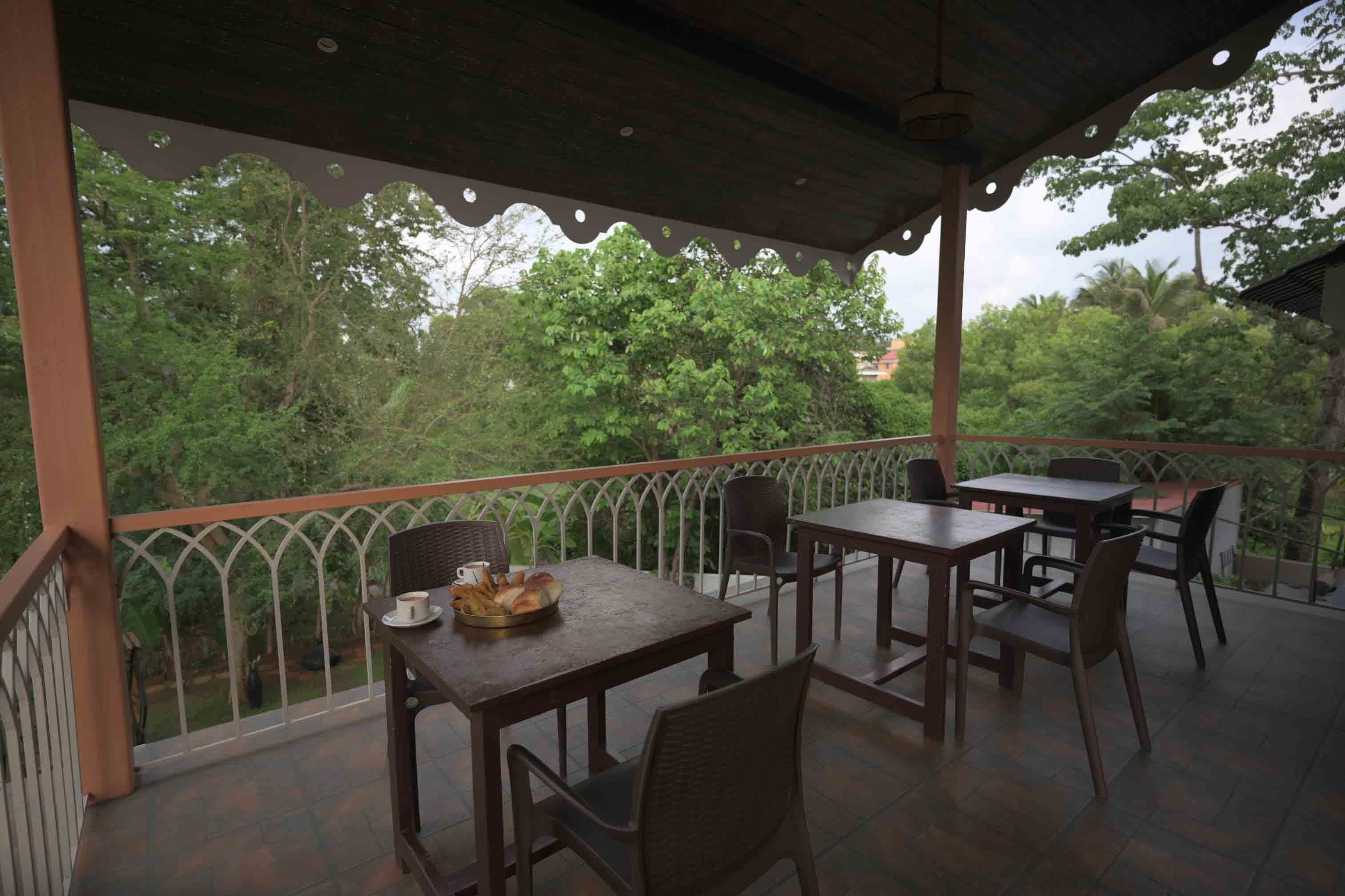 Uma área de estar coberta ao ar livre, com mesas e cadeiras, com vista para um jardim exuberante.