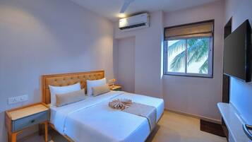 Un dormitorio con cama, mesita de noche, televisor montado en la pared, aire acondicionado y ventana con vistas a palmeras.