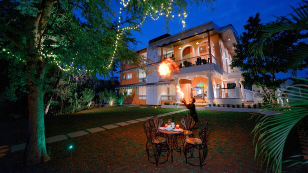 A two-story house with a balcony, surrounded by trees and a well-lit outdoor area with a table and chairs. - Foxoso Vega, Colva, Goa (Margao)