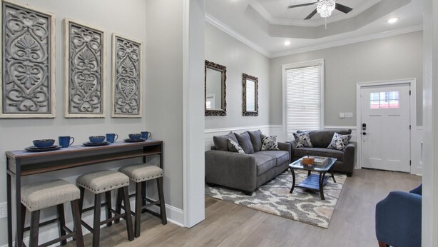 A modern living room with a gray sofa, a coffee table, and a dining area with stools and blue cups.