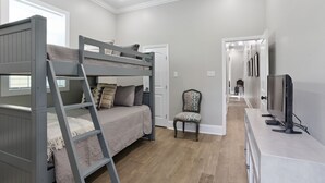 A bedroom with a bunk bed, a chair, a TV, and a hallway leading to another room.
