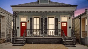 A two-story house with a front porch, two red doors, and a small staircase leading to the entrance.