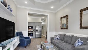 A modern living room with a flat-screen TV, a blue armchair, a grey sofa, and a glass coffee table.