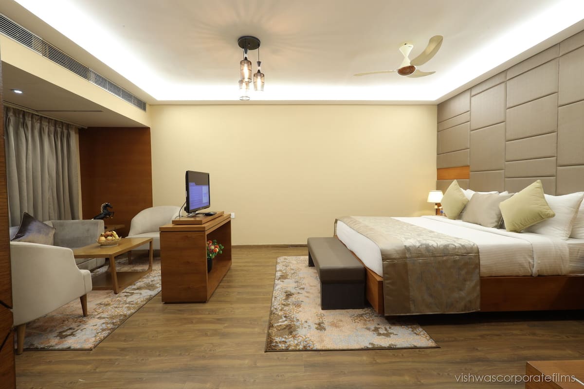 Quarto de hotel moderno com cama, escrivaninha, cadeira, sofá e ventoinha no teto.