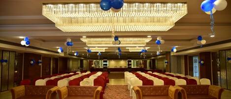 A banquet hall with rows of red and white chairs, a patterned carpet, and a large chandelier.