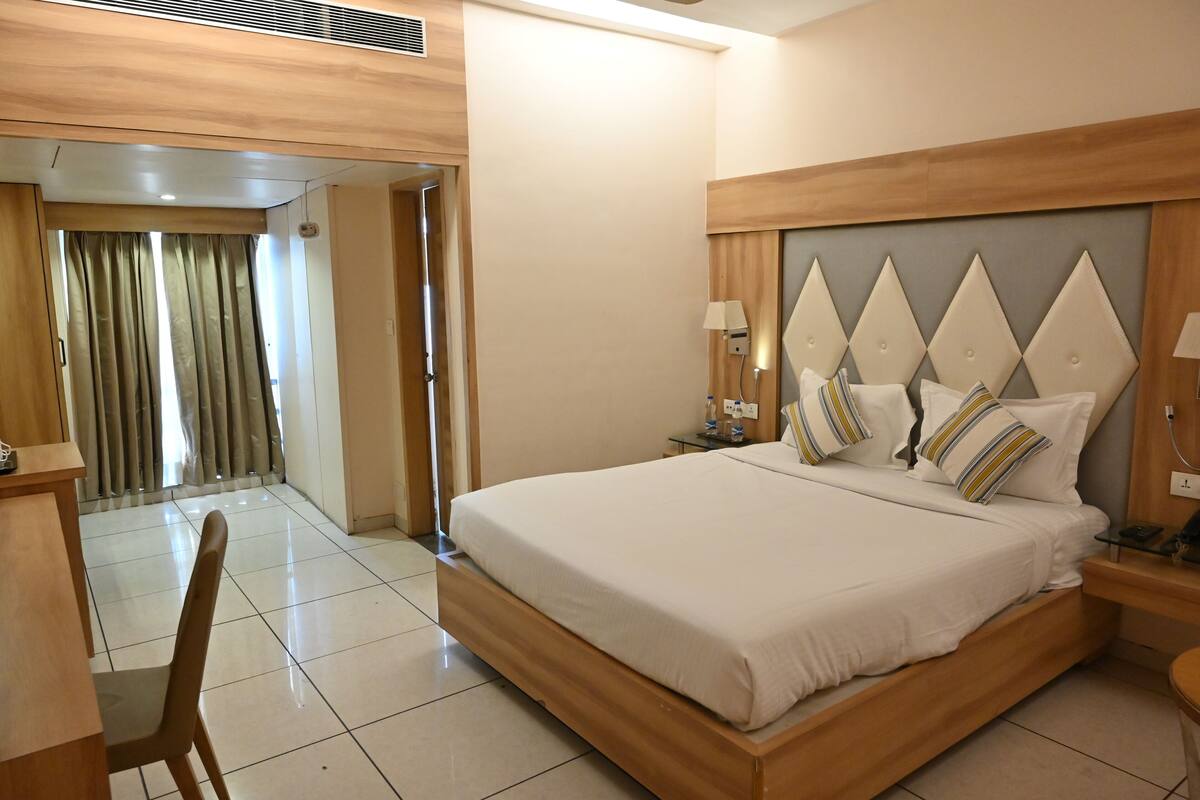 Quarto de hotel com uma cama grande, uma escrivaninha e uma cadeira. Há uma porta que dá para uma varanda.