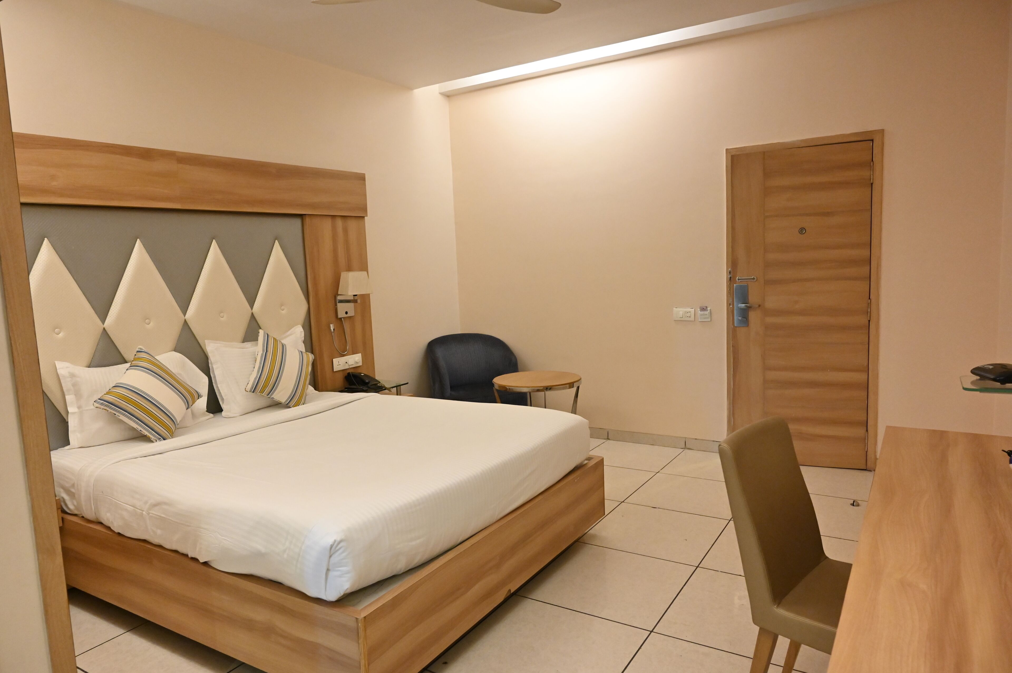 A hotel room with a bed, a desk, a chair, a small round table, and a door.