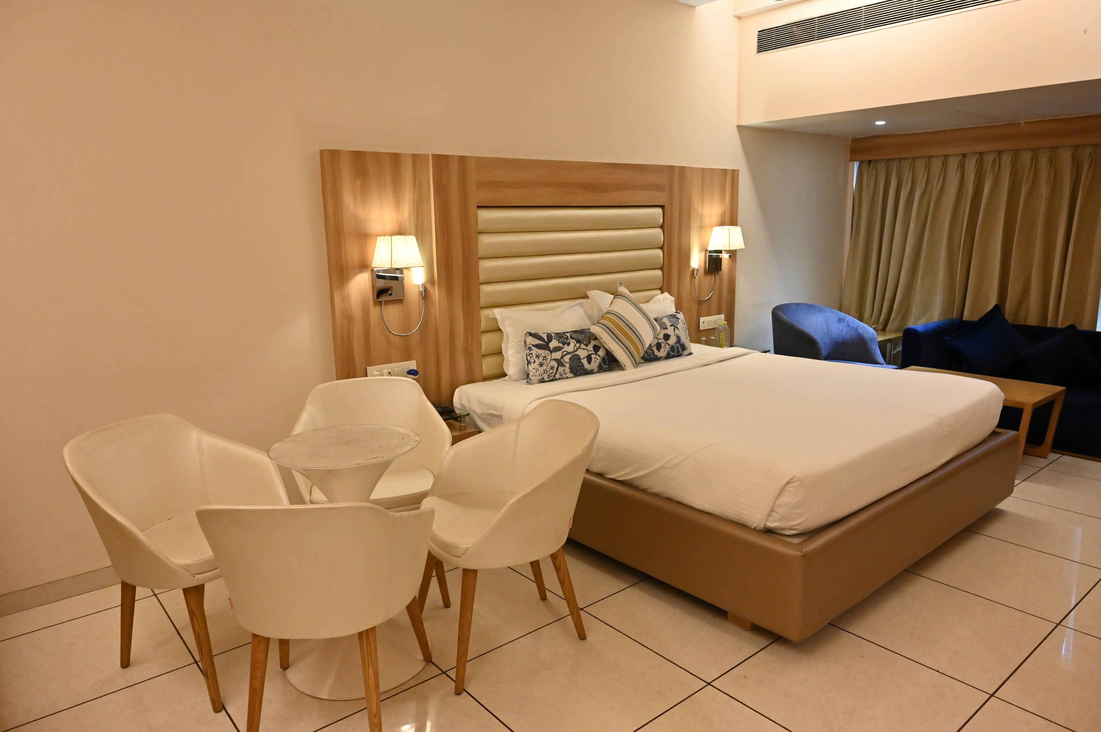 A hotel room with a large bed, two bedside tables, a desk with chairs, and a blue armchair.