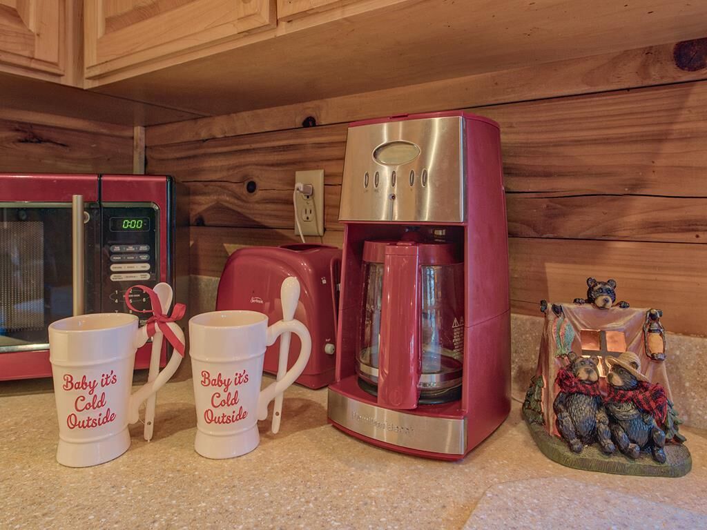 A kitchen with a red microwave, a red coffee maker, and two white mugs with text.