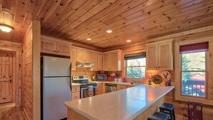 Cocina de cabaña de madera con una isla central, armarios de madera, un refrigerador, un microondas y un lavamanos.