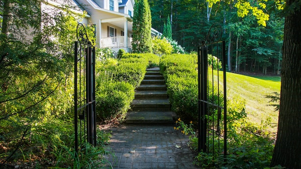 Une maison avec un escalier en pierre menant à la porte d’entrée, entourée d’une végétation luxuriante et d’une pelouse bien entretenue.