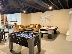 A room with a foosball table, a sofa, a coffee table, and a map on the wall.