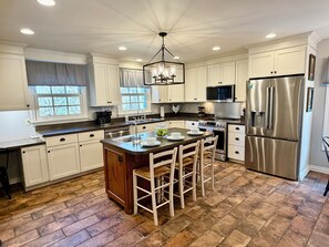 A kitchen with white cabinets, a central island with bar stools, stainless steel appliances, and a chandelier.