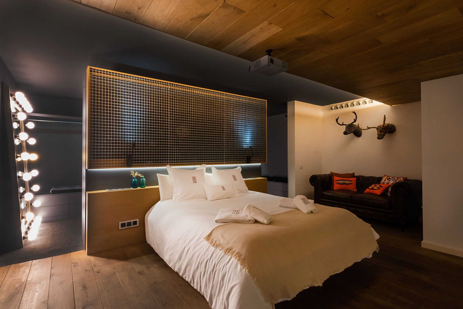 Un dormitorio moderno con una cama grande, un tocador con luces, techo de madera y un adorno de pared.
