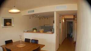 A dining area with a wooden table and chairs, a kitchen with cabinets and a countertop, and a hallway leading to another room. - Modern Apartment - Gardens/Pool/WIFI/AIRCON/PARKING - D302, Apartment Riells Blau D302 in L'Escala -... (L'Escala)