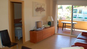 A hotel room with a balcony, a TV on a wooden cabinet, a red sofa, and a painting on the wall. - Modern Apartment - Gardens/Pool/WIFI/AIRCON/PARKING - D302, Apartment Riells Blau D302 in L'Escala -... (L'Escala)