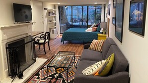 A modern living room with a fireplace, a sofa, a coffee table, and a large bed with a view to the outside.