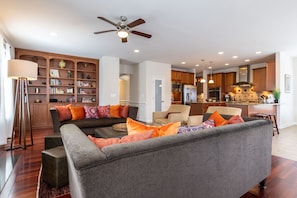 Relax in this stylish living space with a sofa, armchair, and floor lamp, surrounded by a bookshelf and kitchen area.