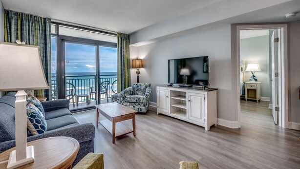 Un salon moderne avec un canapé, une table basse, un téléviseur et un balcon offrant une vue sur l’océan.