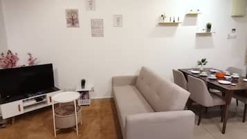 A living room with a sofa, a TV, a dining table with chairs, and a small side table.