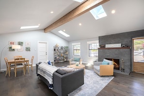 Een ruime woonkamer met een open haard, een eethoek met houten meubels en een groot raam dat natuurlijk licht binnenlaat.