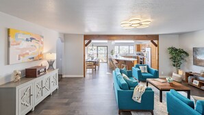 Ein geräumiges Wohnzimmer mit einer Couch, Sesseln und einem Couchtisch. Im Hintergrund ist eine Essecke mit Tisch und Stühlen erkennbar.