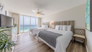 Habitación de hotel con una cama grande, televisor, ventilador de techo y vista al océano.