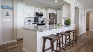 Una cocina moderna con armarios blancos, una isla central con taburetes, un microondas y un refrigerador.