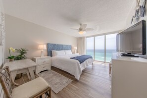 Un dormitorio con cama, mesitas de noche, escritorio, silla, televisor y vista al océano.