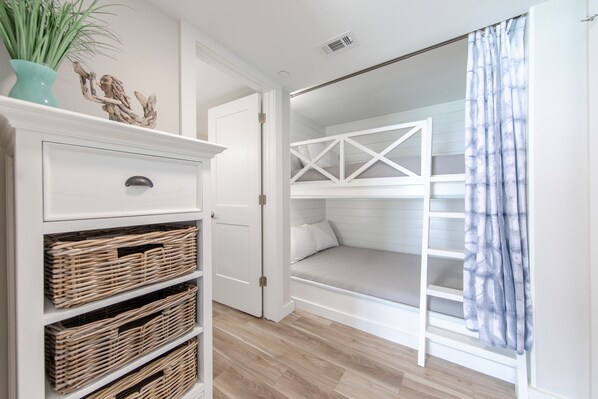 A room with a white bunk bed, a white dresser with wicker baskets, and a potted plant.