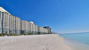 Un hotel frente a la playa con varios edificios altos, una playa de arena y un cielo azul despejado.