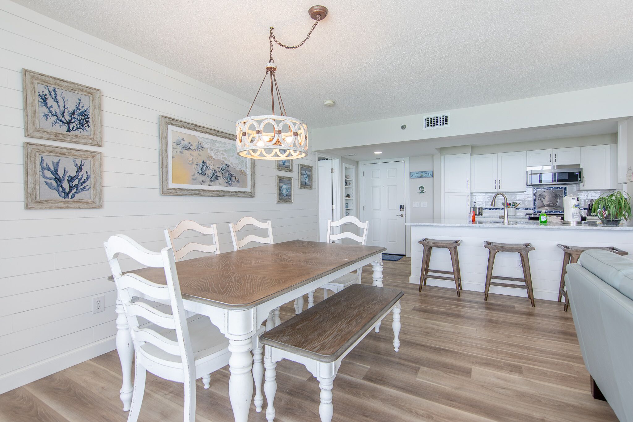 A dining area with a wooden table and white chairs, a bench, and a hanging light fixture.