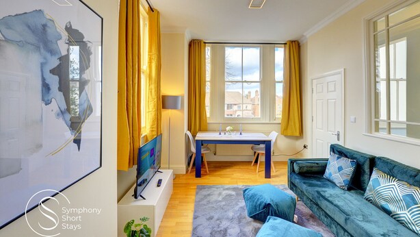A modern living room with a blue sofa, a dining table, and a TV. - Beautiful, light & spacious Regency 2 bed apt (Royal Leamington Spa)