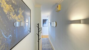 A hallway with a large abstract painting, a black floor lamp, a rug, and a wall-mounted mirror. - Beautiful, light & spacious Regency 2 bed apt (Royal Leamington Spa)
