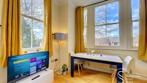 A modern living room with a flat-screen TV, a desk, and a chair. - Beautiful, light & spacious Regency 2 bed apt (Royal Leamington Spa)