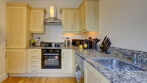 A compact kitchen with wooden cabinets, a built-in oven, a microwave, a coffee maker, and a sink. - Beautiful, light & spacious Regency 2 bed apt (Royal Leamington Spa)