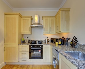 A compact kitchen with wooden cabinets, a built-in oven, a microwave, a coffee maker, and a sink.