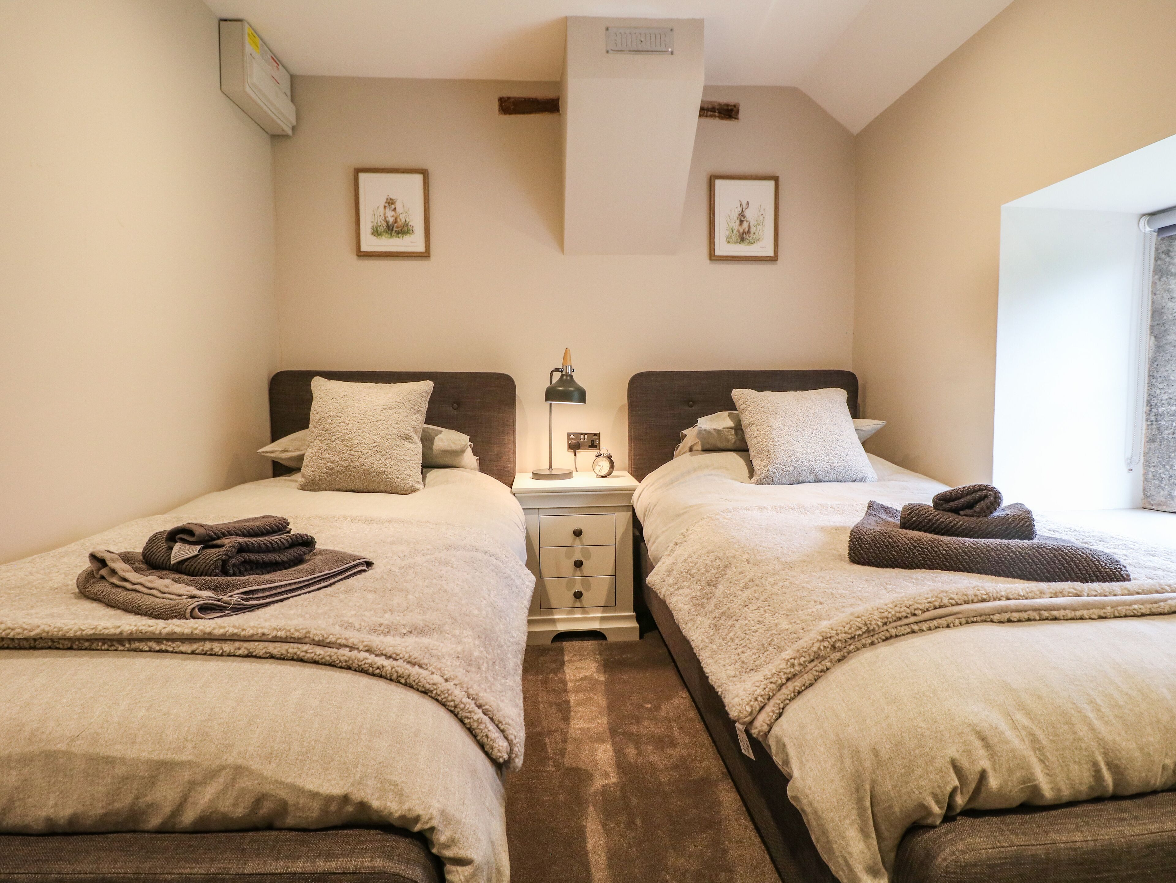 Habitación doble con dos camas, una mesita de noche con lámpara y dos cuadros enmarcados en la pared.