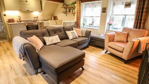 Una sala acogedora con un sofá seccional, una chaise lounge y una cocina al fondo.