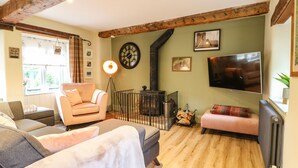 Una sala de estar acogedora con un sofá, un sillón, un reposapiés, una chimenea, un televisor y un reloj en la pared.