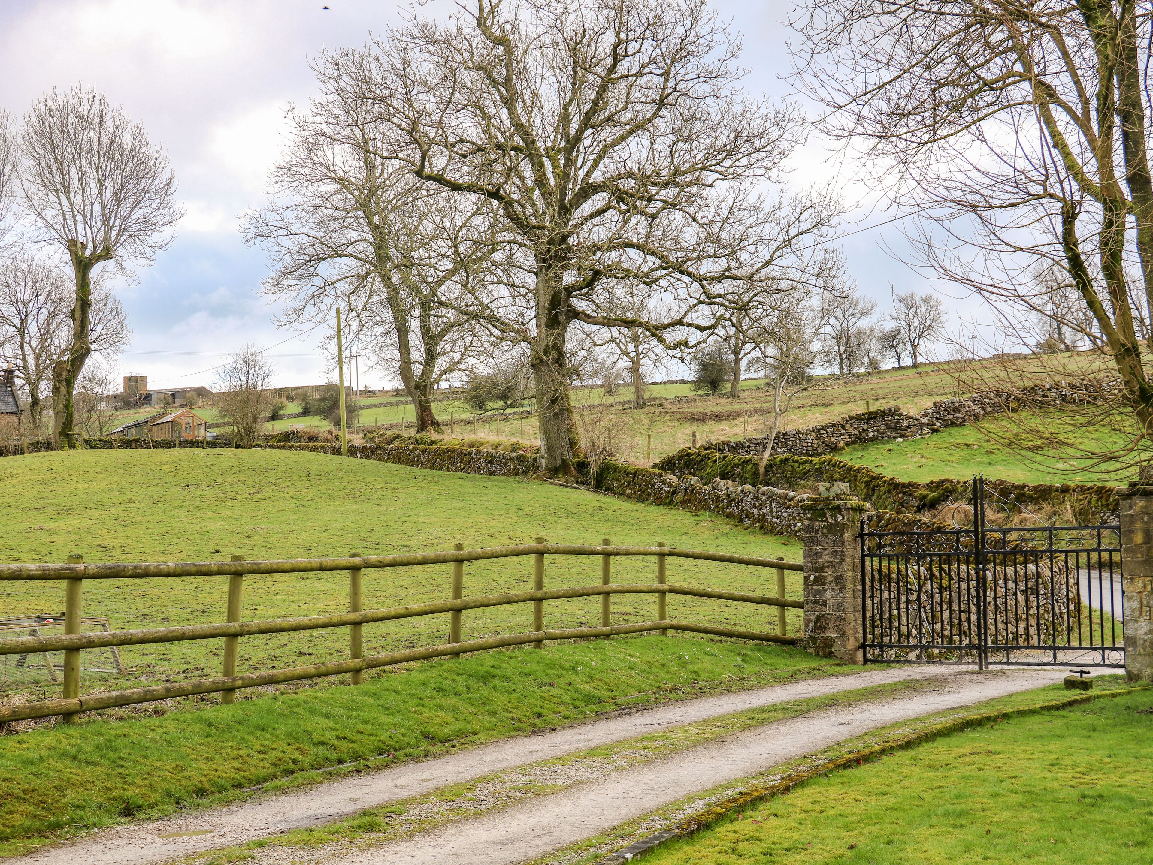 A rural landscape with a stone wall, a wooden fence, and a gate leading to a path.