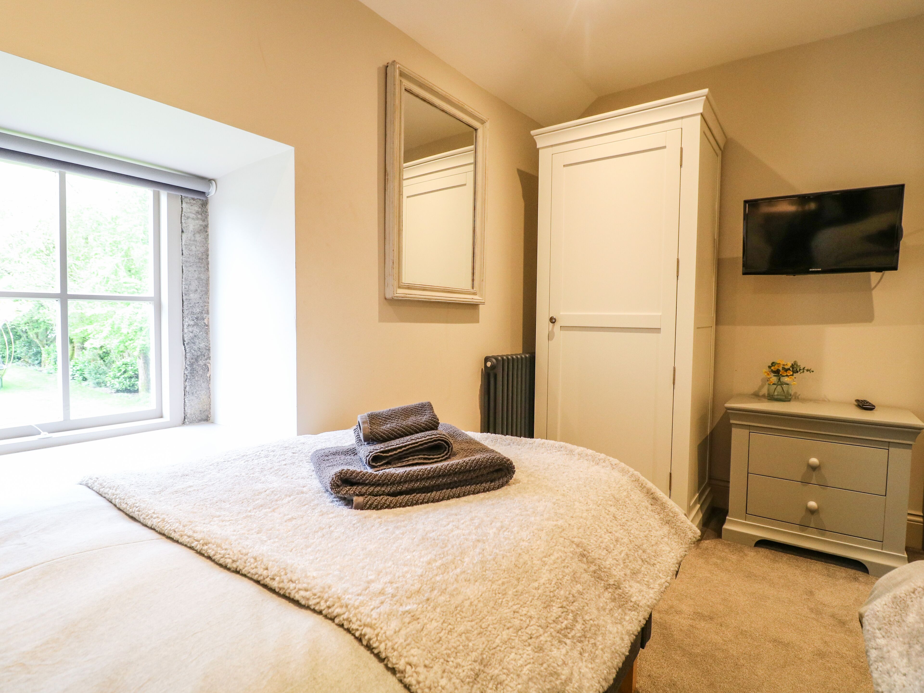 A bedroom with a bed, a dresser, a TV, and a window with a view of greenery.