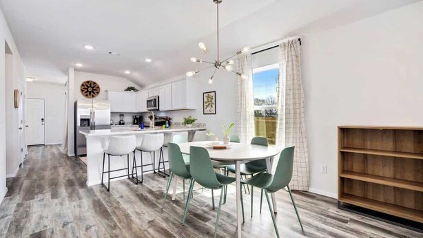 Una cocina moderna con armarios blancos, una isla central y una zona de comedor con sillas verdes.