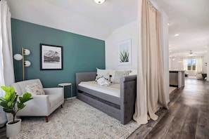 A modern living room with a sofa, a bed, a small side table, and a potted plant.