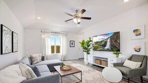 Una sala de estar moderna con un sofá, un sillón, una mesa de centro y un televisor de pantalla plana.