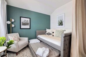 A bedroom with a bed, a sofa, a chair, and a small table with a plant.