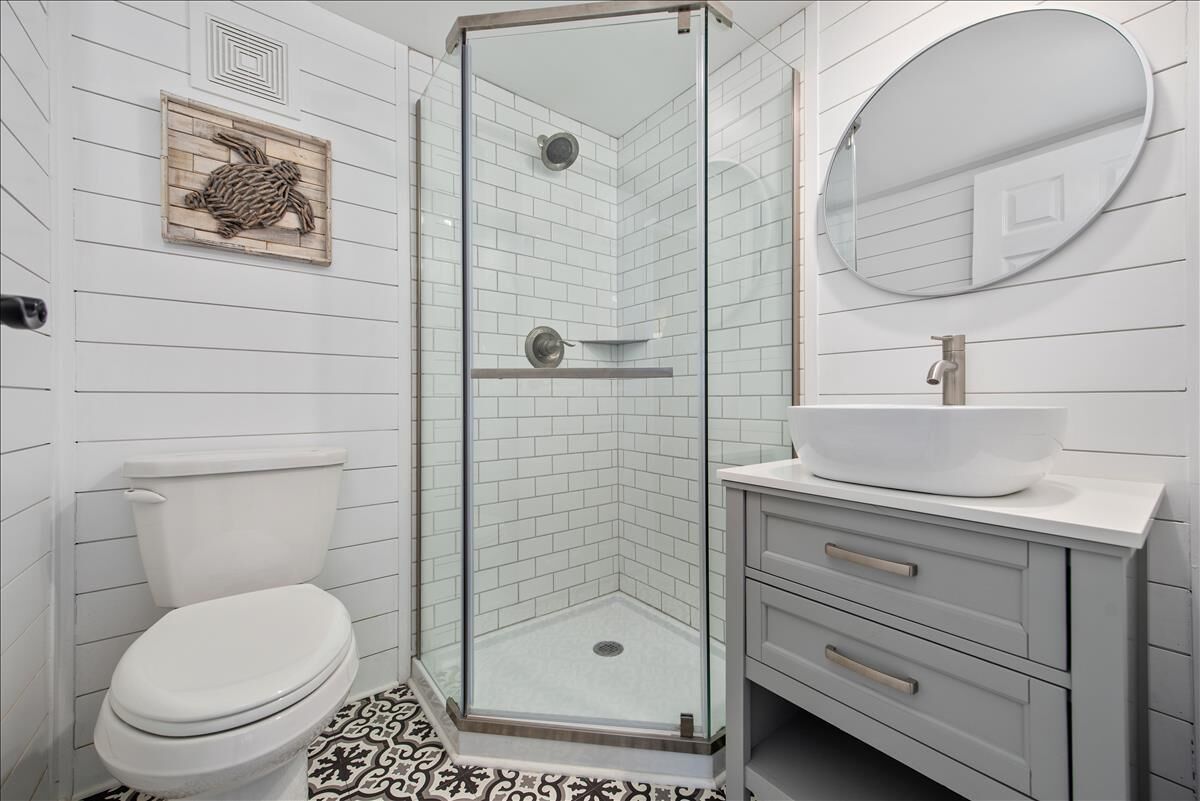Ein Badezimmer mit Duschkabine, Toilette in Weiß, Waschbecken mit Aufsatzbecken und einem Spiegel darüber.