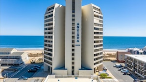 Un edificio alto y moderno con el nombre "ANTIGUA" en su fachada, situado cerca de una playa con vista clara al océano.