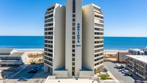 Un edificio alto y moderno con el nombre "ANTIGUA" en su fachada, situado cerca de una playa con vista clara al océano.