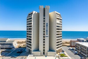 A tall, modern building with the name "ANTIGUA" on its facade, located near a beach with a clear view of the ocean.